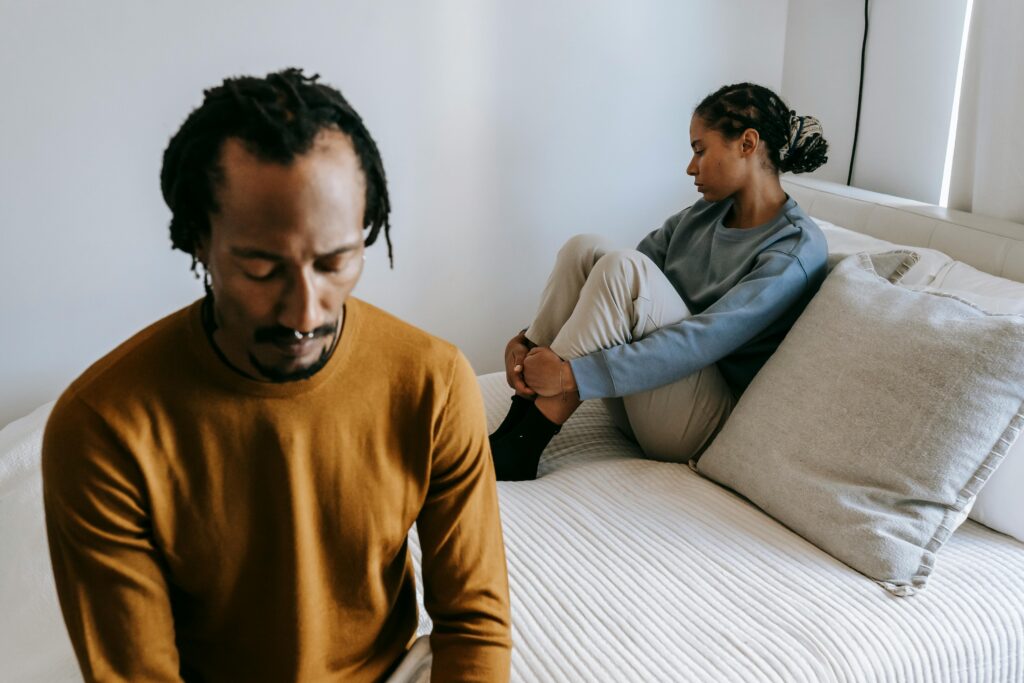 Young black couple in casual outfit spending time on bed with sad face in daytime at home