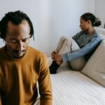 Young black couple in casual outfit spending time on bed with sad face in daytime at home