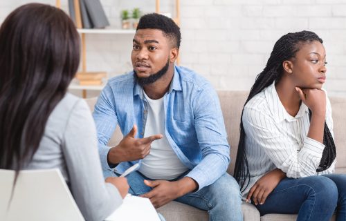 Afro Husband Sharing Family Problems Sitting Next To His Offended Wife At Counselor's Office, Selective Focus