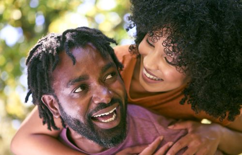 Loving Mid Adult Couple Outdoors In Summer Garden Or Countryside With Man Giving Woman Piggyback