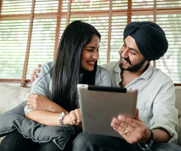A joyful couple using a tablet indoors, embracing and smiling together.