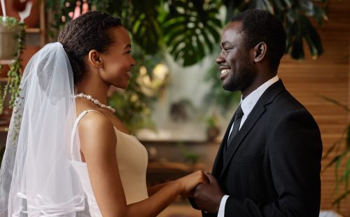 Waist up portrait of young black couple getting married and looking at each other holding hands