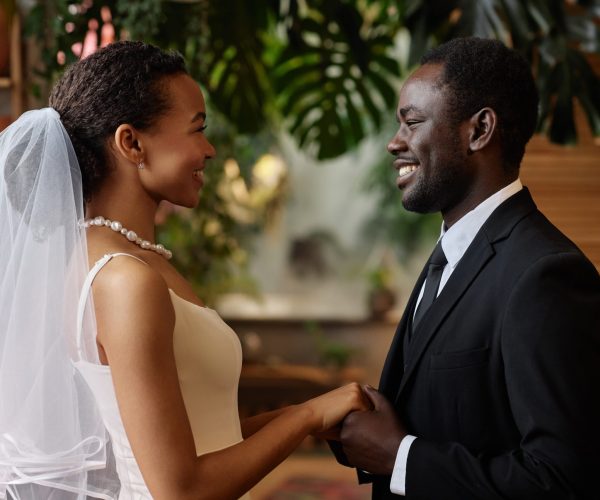 Waist up portrait of young black couple getting married and looking at each other holding hands